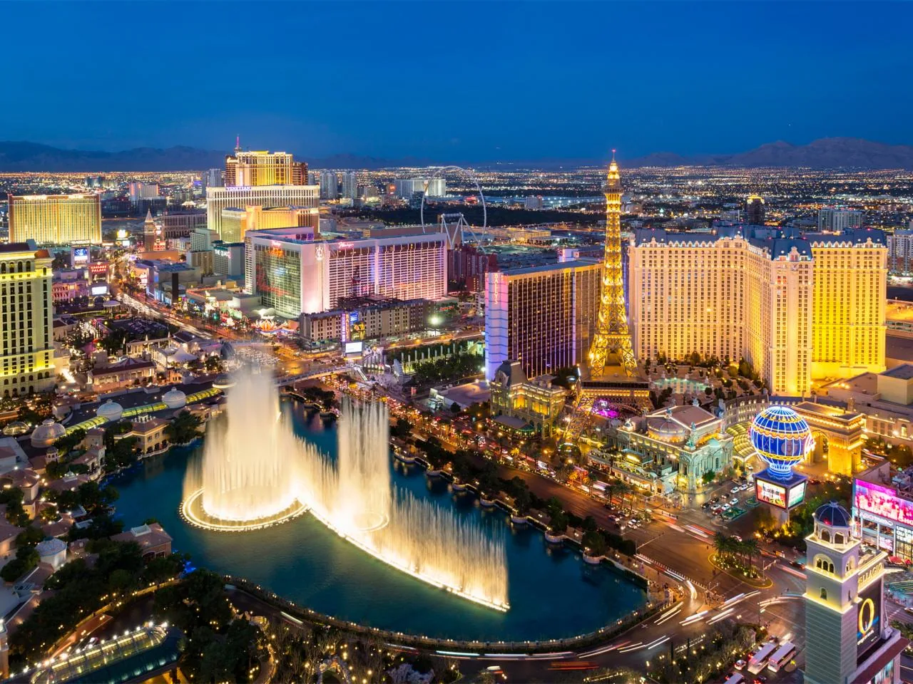 Las Vegas Strip skyline at night with illuminated fountains, hotels, and Eiffel Tower replica.