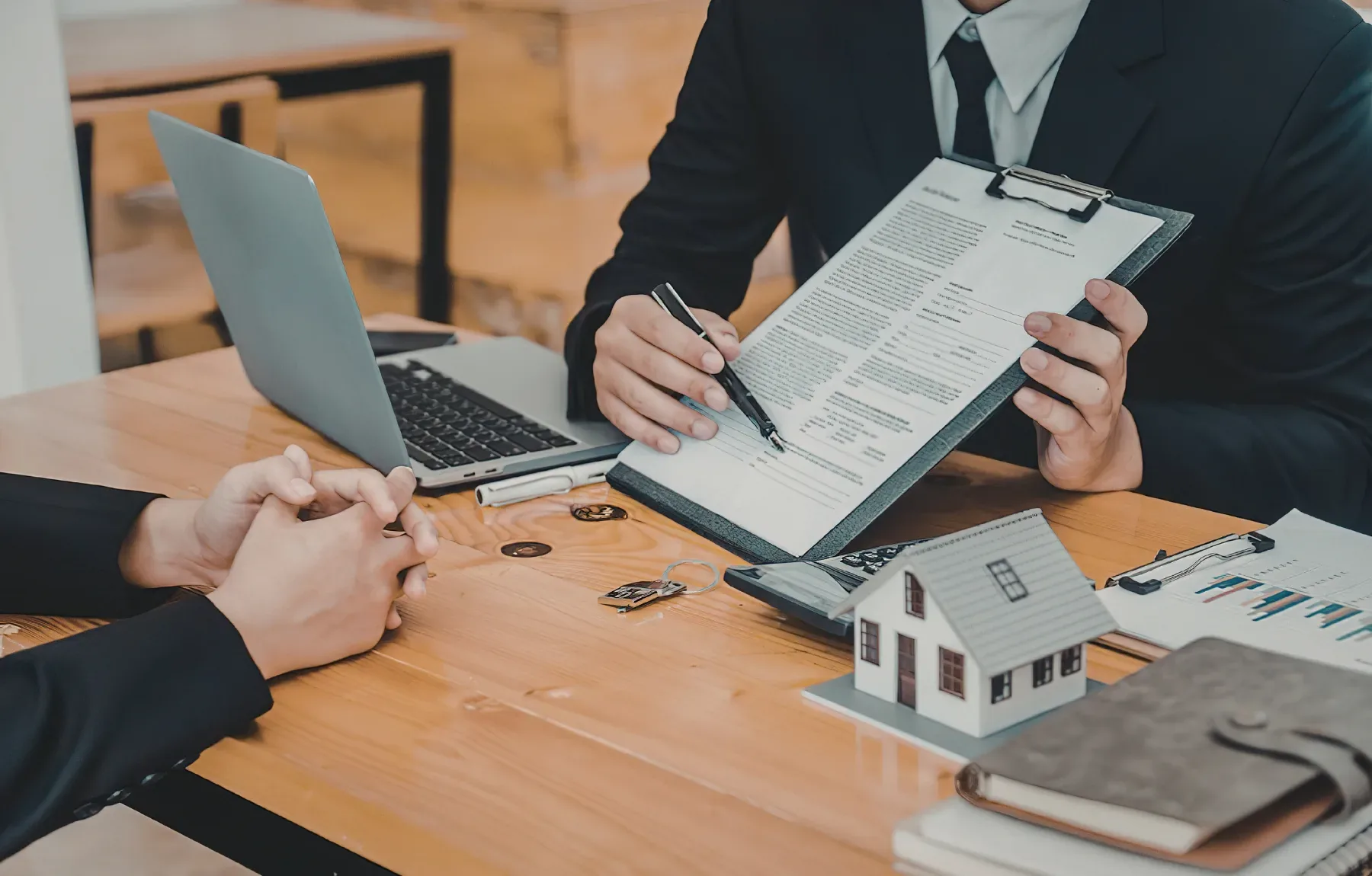 Property manager reviewing rental agreement and contract documents with client at wooden desk during consultation meeting.