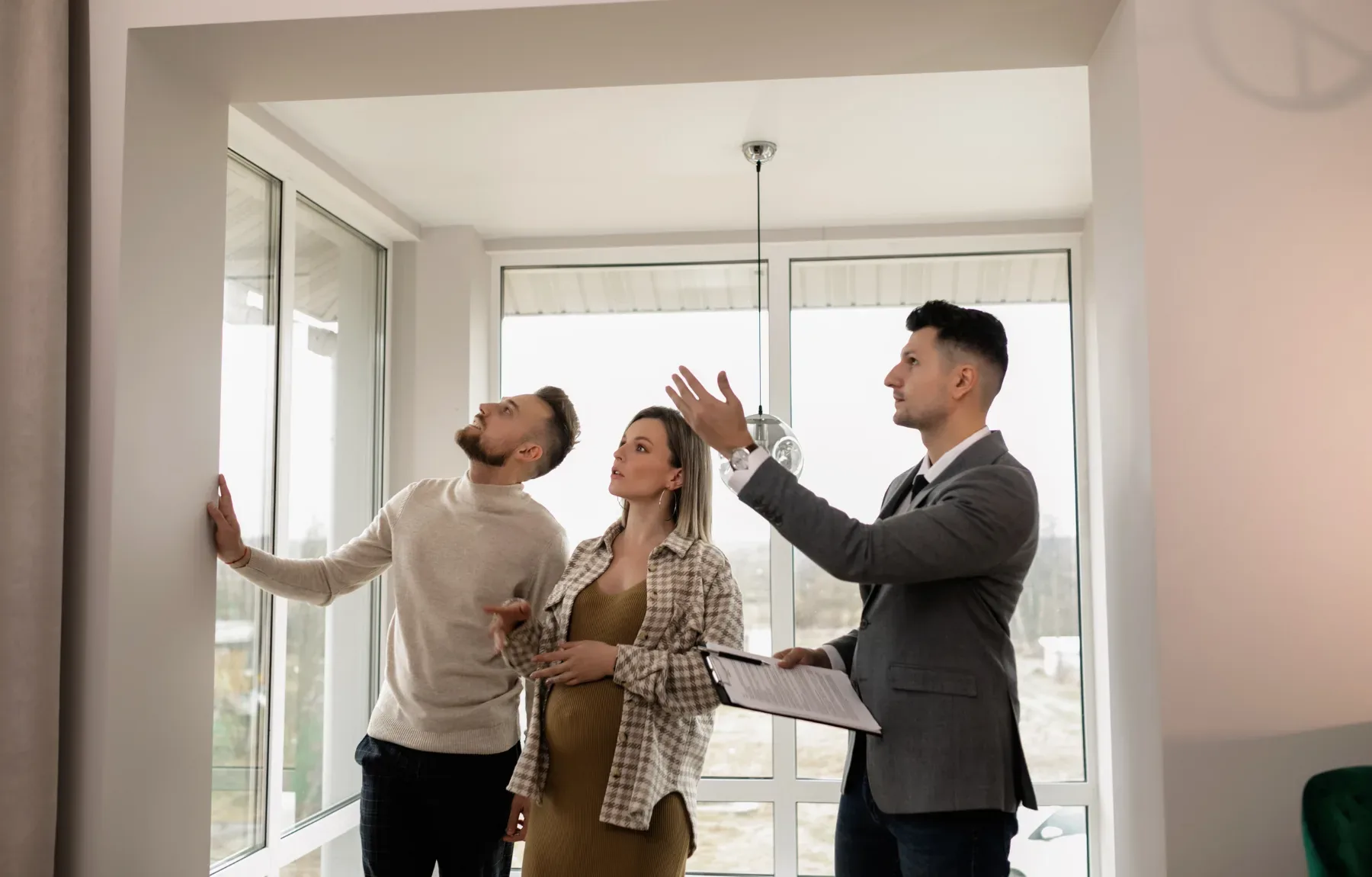 A real estate agent or property manager shows a young couple their new apartment, pointing out ceiling features while reviewi