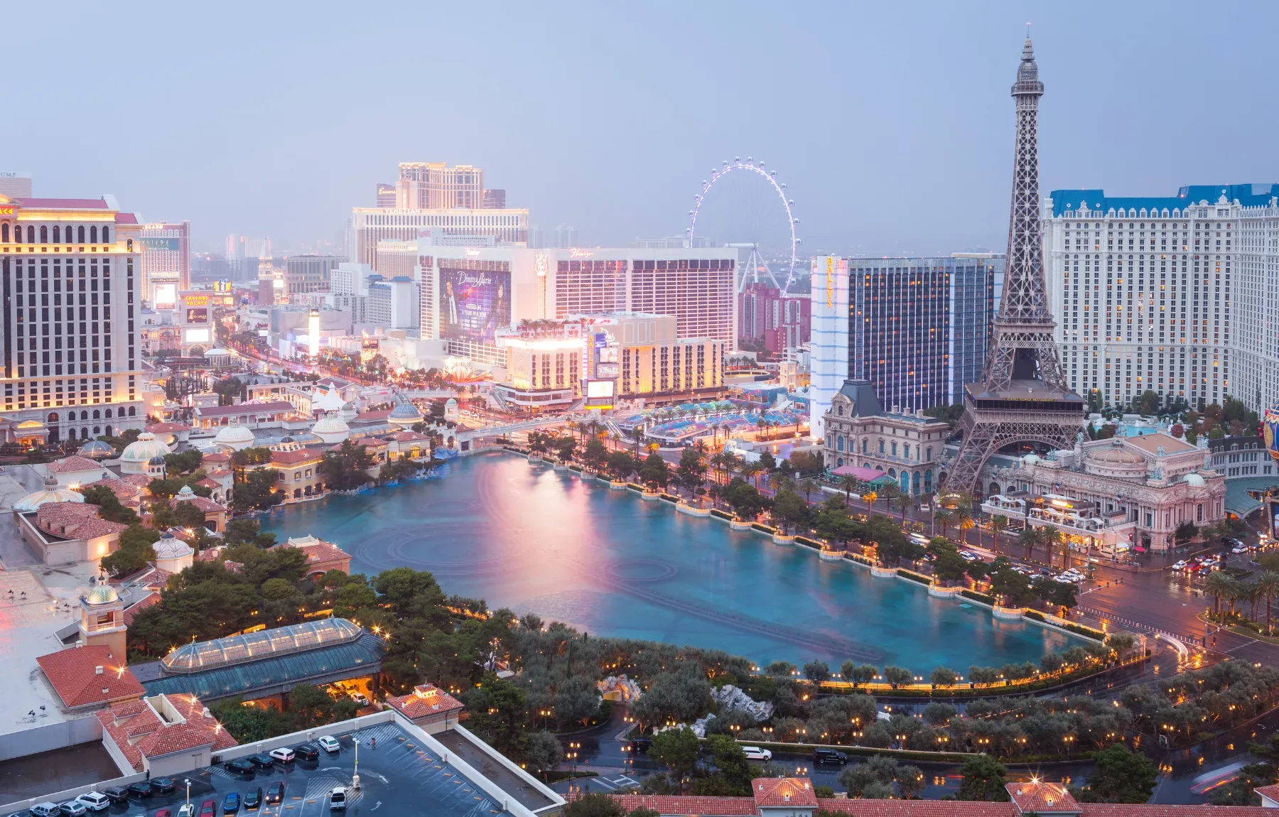 Twilight aerial view of a Las Vegas resort with illuminated fountains, manicured landscapes, and pristine water features show
