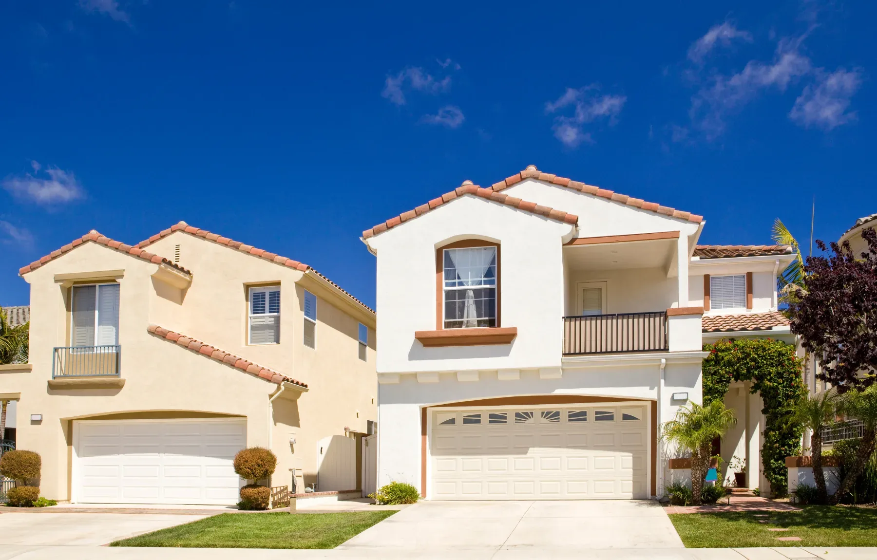 Two beautiful Mediterranean-style homes with cream and white stucco exteriors, terracotta tile roofs, and manicured landscapi